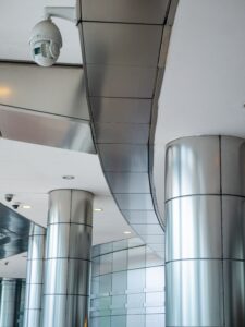 Ceiling-mounted CCTV surveillance cameras in a modern commercial building with metallic columns and contemporary interior architecture.